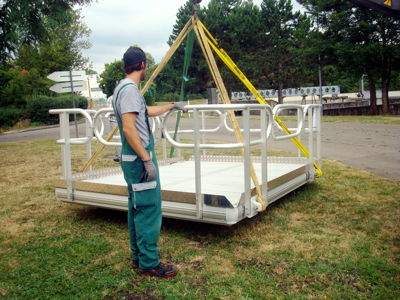 EasyFloat arbetsflotte med räcken lyfts av kran med vajrar, medan en arbetare står på land och håller i flotten under säker hantering.