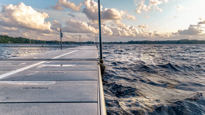 Närbild på en lång EasyFloat offentlig badbrygga med dramatiska moln ovanför och lätt vågigt vatten.